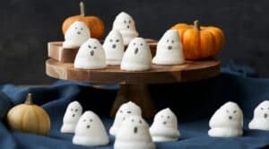 Cute ghost Halloween decorations made from marshmallows with adorable faces, displayed on a wooden cake stand.